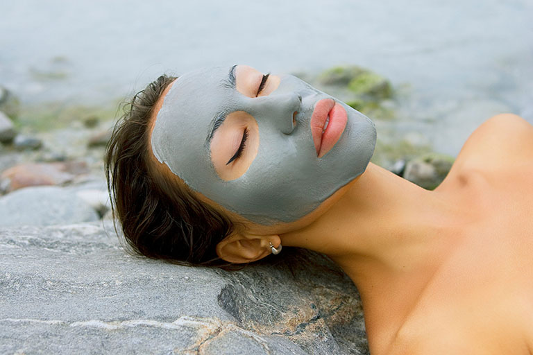 Woman with blue clay facial mask in beauty spa (wellness).